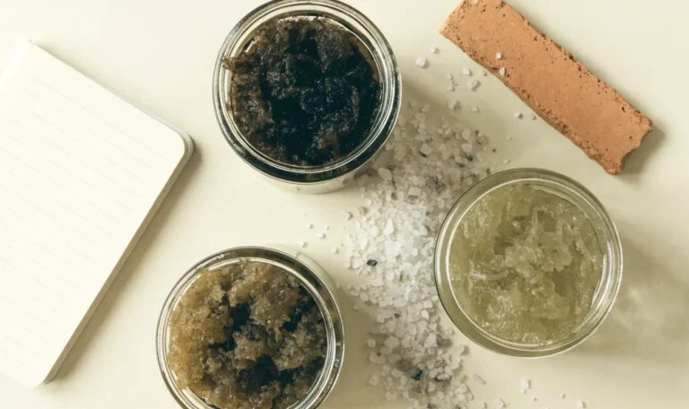 An unbranded flat lay comparing three plain glass jars of sea moss gel of different shades on a pale cream surface with a notebook, illustrating alodi sea moss.