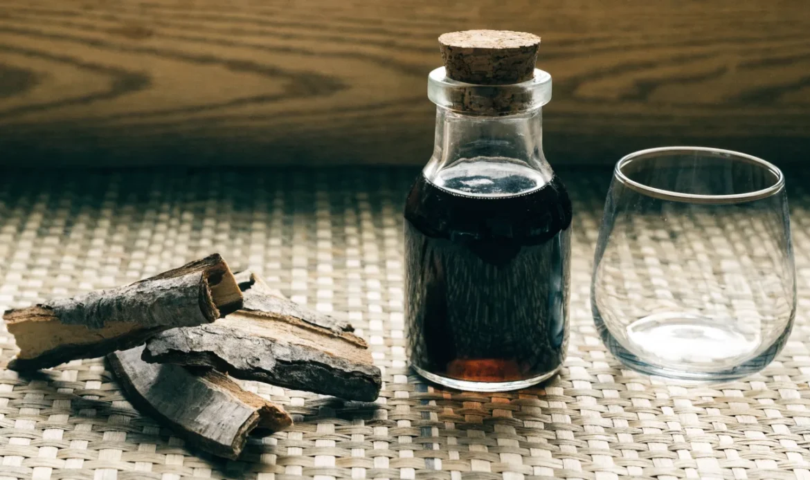 Strips of rough bois bande tree bark and a small bottle of dark infusion on a woven Caribbean mat, illustrating bois bande.