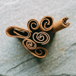 Ceylon cinnamon quills on pale grey stone, two snapped open to show the fine papery concentric layers that identify true cinnamon
