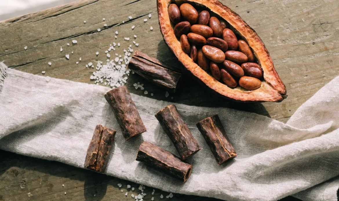 Hand-rolled Caribbean cocoa sticks and a split cocoa pod with glossy beans on a rough wooden table, illustrating cocoa de.