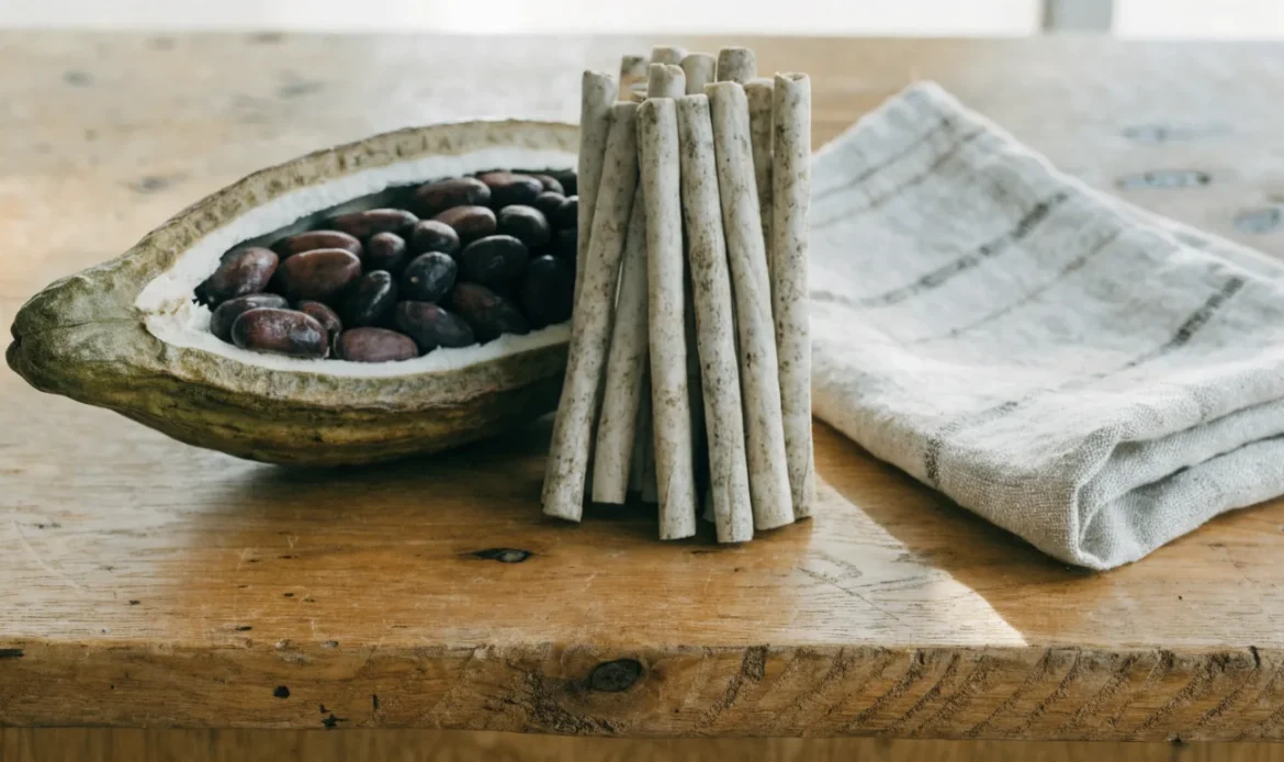 Hand-rolled Caribbean cocoa sticks and a split cocoa pod with glossy beans on a rough wooden table, illustrating cocoa spheres.