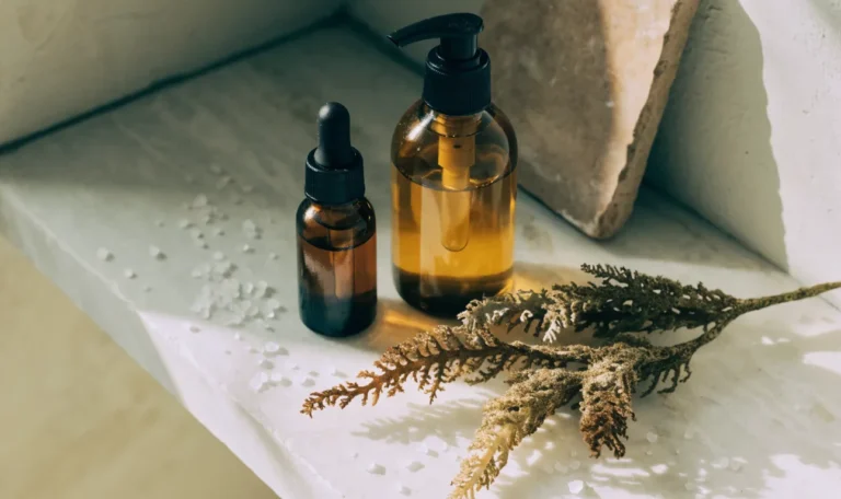 Unlabelled amber glass bottles of hair oil and cleanser on a pale stone bathroom shelf, a sprig of dried sea moss beside them, illustrating deep condition sea moss.