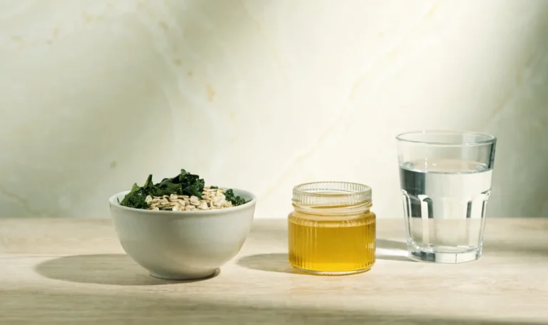 A simple bowl of oats and greens with a small jar of golden gel and a glass of water on a light wooden table, illustrating does sea moss have fiber.