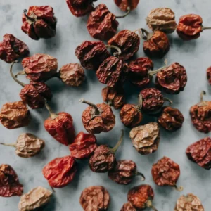Dried scotch bonnet chillies on pale grey stone, small wrinkled lantern-shaped peppers in deep red and burnt orange