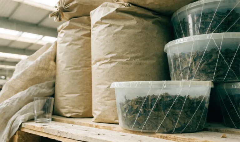 Stacked kraft sacks and sealed food-grade tubs of dried seaweed on a clean warehouse pallet, soft industrial daylight, illustrating how to order sea moss.