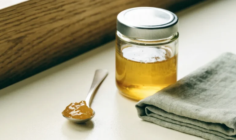 A small measured spoonful of golden sea moss gel beside a closed glass jar on a pale cream surface, restrained clinical styling, illustrating is sea moss from st lucia safe.