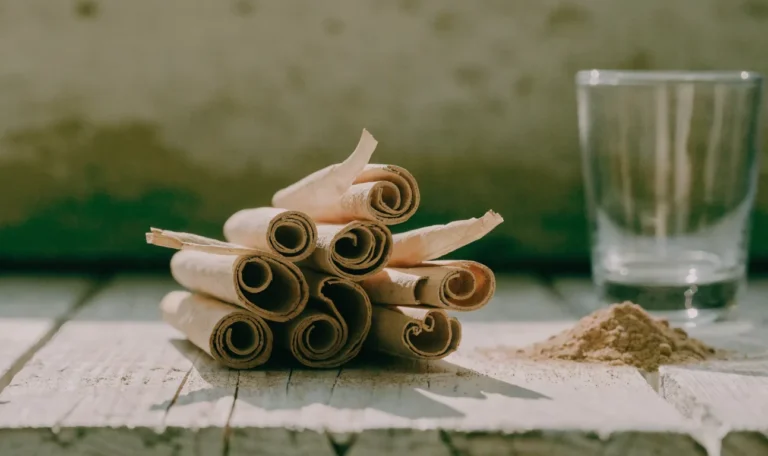 A loose bundle of pale, fragile, many-layered Ceylon cinnamon quills on a rustic wooden board with a small heap of ground cinnamon, illustrating penzeys ceylon cinnamon.