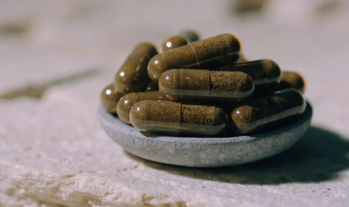 Amber vegetable capsules of sea moss powder in a small stone dish on a pale surface