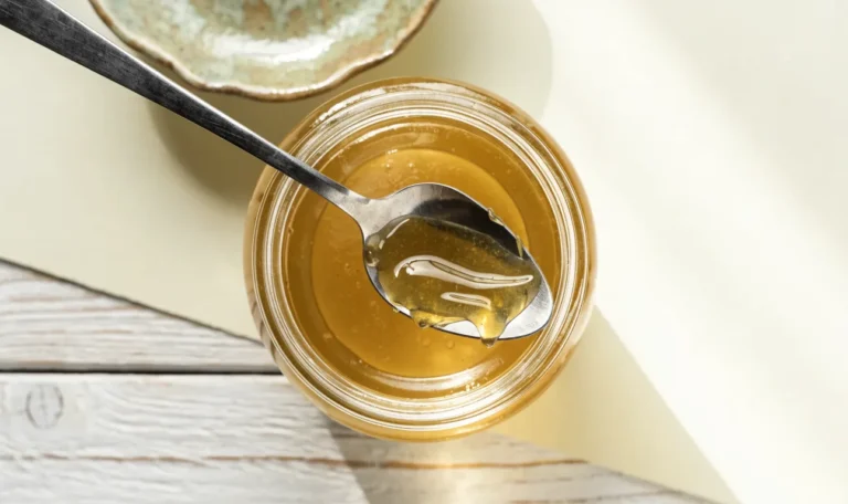 A clear glass jar of translucent golden sea moss gel with a spoon lifting a thick ribbon of it, cream backdrop, illustrating sea moss gel recipe.