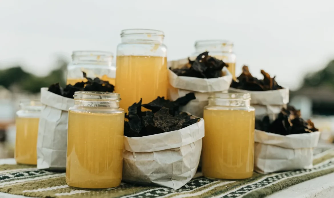 An unbranded market stall table of glass jars of golden gel and paper bags of dried seaweed under soft daylight, illustrating sea moss near me.