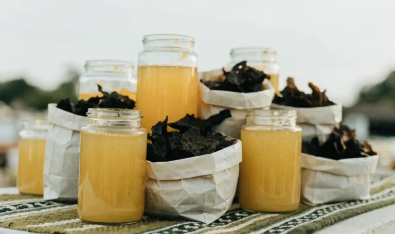 An unbranded market stall table of glass jars of golden gel and paper bags of dried seaweed under soft daylight, illustrating sea moss near me.