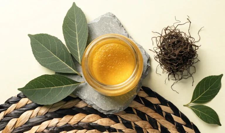 A still life of a glass jar of golden sea moss gel, a small pile of dried wildcrafted sea moss and fresh green leaves on a pale cream surface, illustrating sea moss taste.