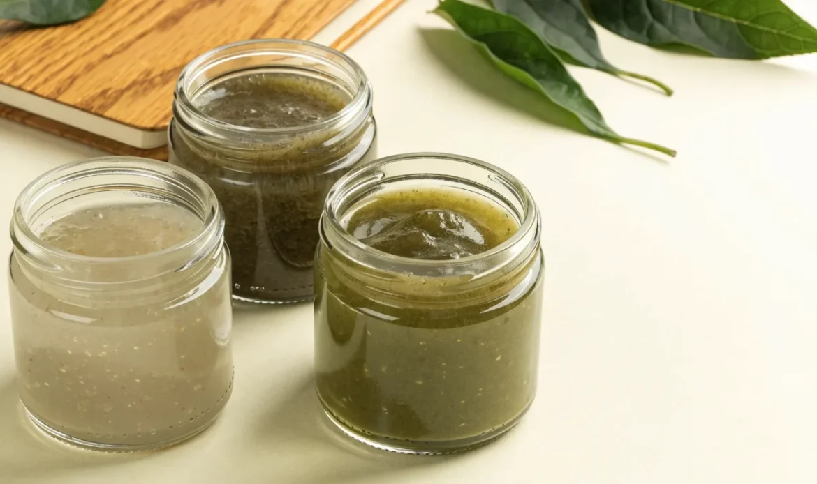 An unbranded flat lay comparing three plain glass jars of sea moss gel of different shades on a pale cream surface with a notebook, illustrating tailormade sea moss.