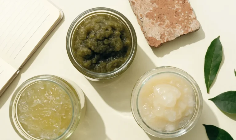 An unbranded flat lay comparing three plain glass jars of sea moss gel of different shades on a pale cream surface with a notebook, illustrating top 10 sea moss brands.