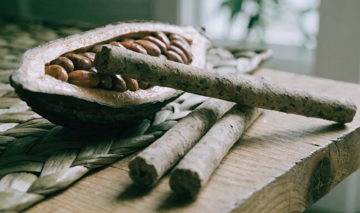 Hand-rolled Caribbean cocoa sticks and a split cocoa pod with glossy beans on a rough wooden table, illustrating trinidad cocoa.