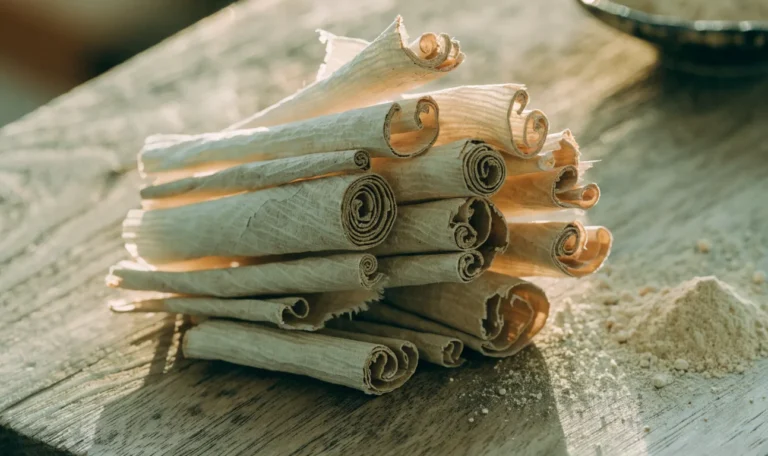 A loose bundle of pale, fragile, many-layered Ceylon cinnamon quills on a rustic wooden board with a small heap of ground cinnamon, illustrating what brands are ceylon cinnamon.